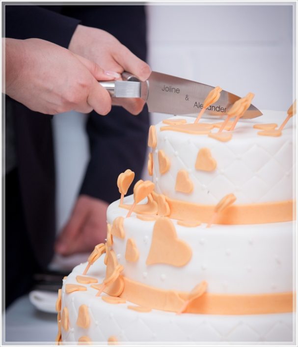 Hochzeitstorte mit orangefarbenem Dekor wird angeschnitten.